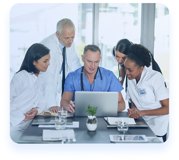 A diverse team of doctors and healthcare professionals collaborating around a laptop during a clinical meeting.